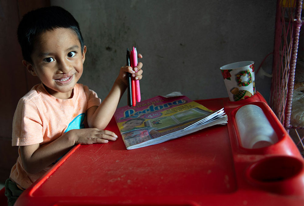 Anghelo smiling and drawing at his desk after cleft surgery