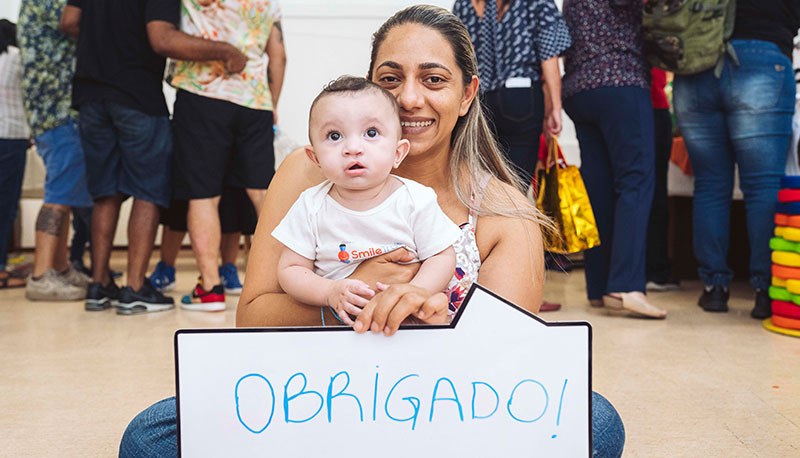Mãe segurando cartaz em português que diz obrigado