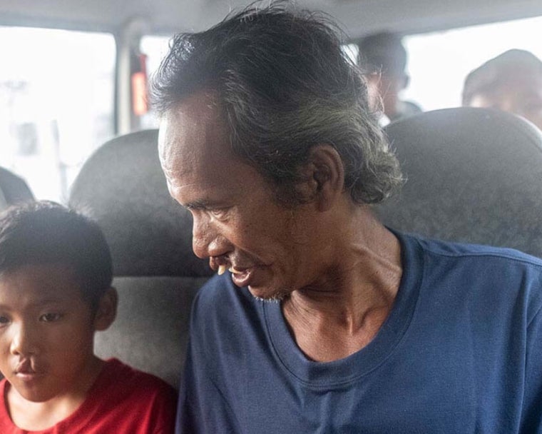 Alim sorrindo e sentado ao lado de Rajib em uma van